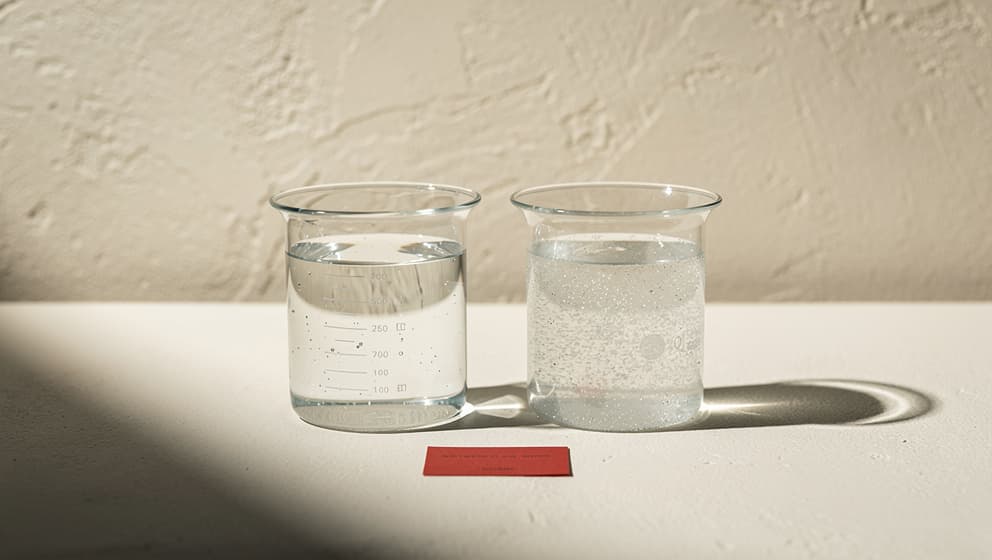 Two transparent glass beakers side by side with same liquid volume but different particle densities, representing discordance between LDL cholesterol mass and ApoB particle count