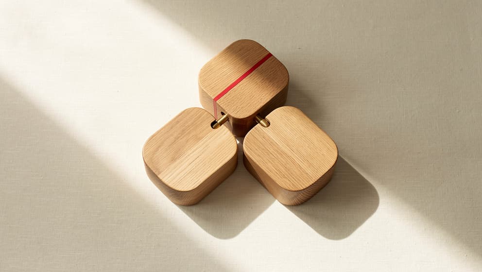 Three interlocking wooden blocks on cream linen, representing the three transformation dimensions of the product operating model: how you build, how you solve, how you decide what to solve